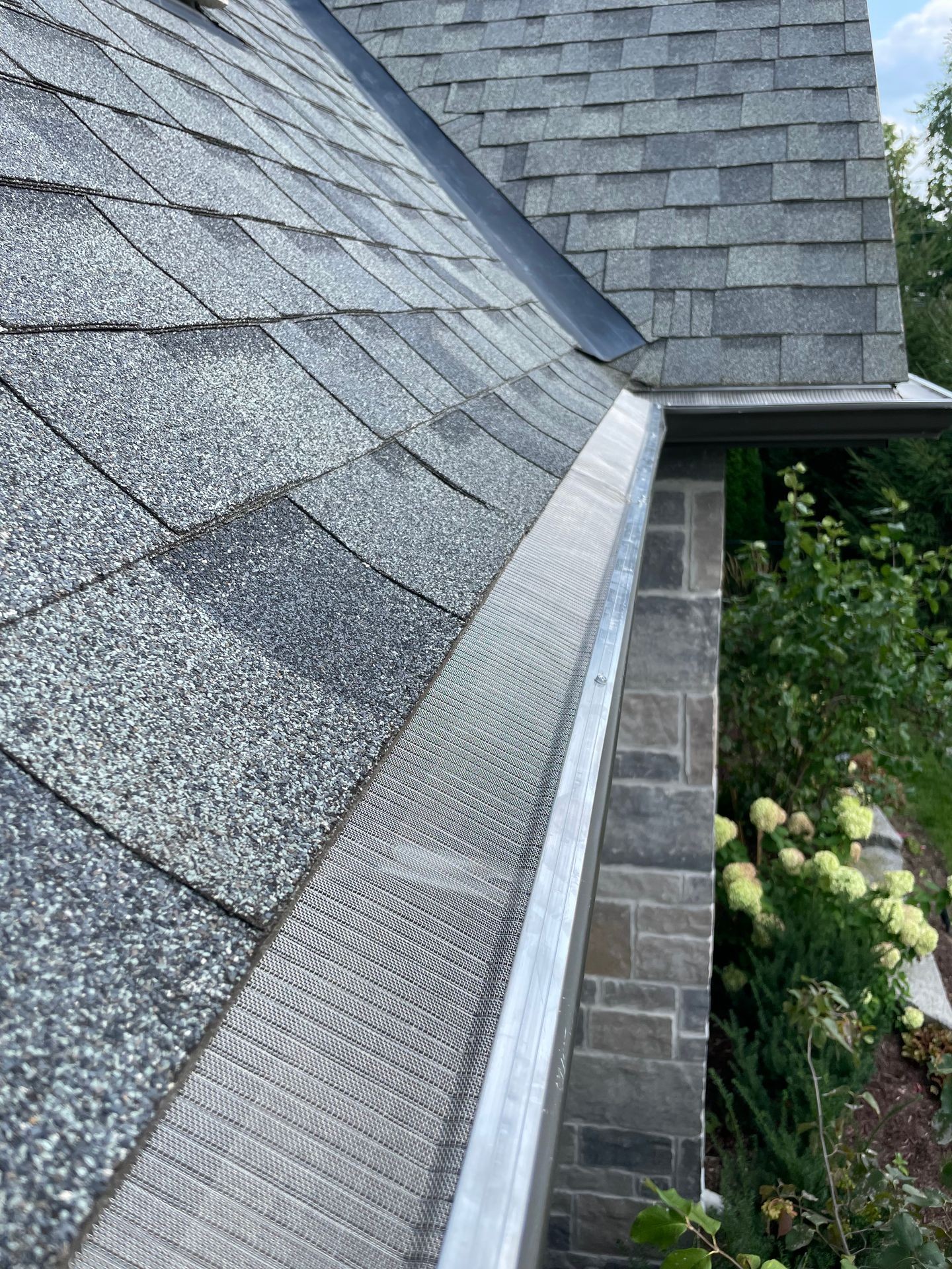 Close-up view of a house roof with gray shingles and a newly installed gutter guard system.