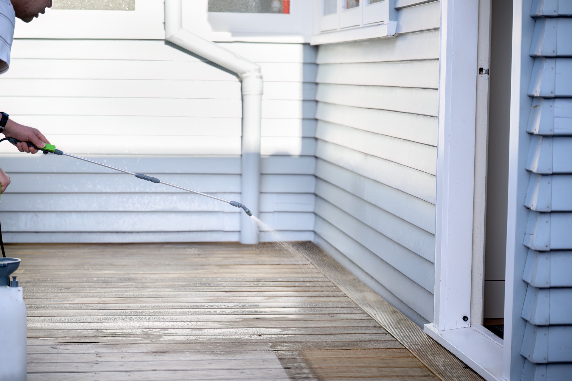 Man cleaning wooden deck with hand-held pressure sprayer. Auckland.